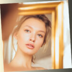 A close-up portrait of a serene young woman looking at her reflection in a golden mirror, symbolizing self-reflection and the search for inner confidence for a psychological quiz.