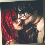 A man and woman in dramatic clown-inspired makeup and costumes, looking intensely at each other in a dark, cinematic setting.