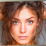 A close-up portrait of a woman with green eyes looking intensely forward while running her hands through her messy, brown hair against a neutral gray background.
