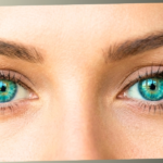 An extreme close-up of a person's vibrant green and turquoise eyes looking directly forward with a focused and slightly self-conscious expression.