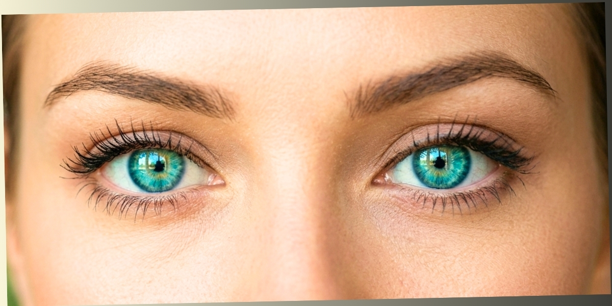 An extreme close-up of a person's vibrant green and turquoise eyes looking directly forward with a focused and slightly self-conscious expression.